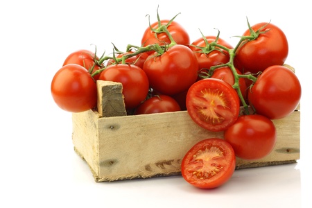 fresh tomatoes on the vine and a cut one in a wooden crate on a white background の写真素材