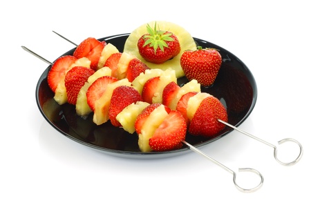 fresh strawberry halves and pieces of pineapple on a skewer on a black plate の写真素材