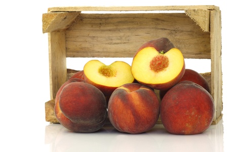 freshly harvested peaches and a cut one in a wooden crate on a white background の写真素材