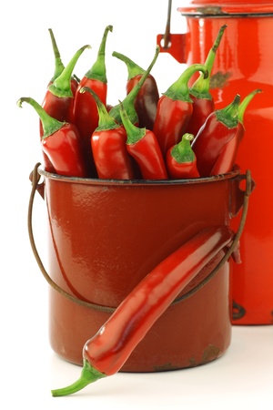 fresh red chili peppers in an old brown enamel cooking pot with red metal coffee pot on background の写真素材
