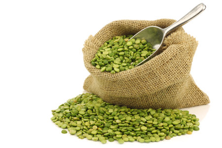 split green peas in a burlap bag with an aluminum scoop on a white background 