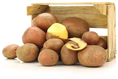 freshly harvested dutch potatoes called  Bildtstar  and a peeled one in a wooden crate on a white background の写真素材
