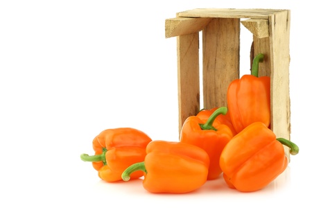fresh orange bell peppers in a wooden crate on a white background の写真素材