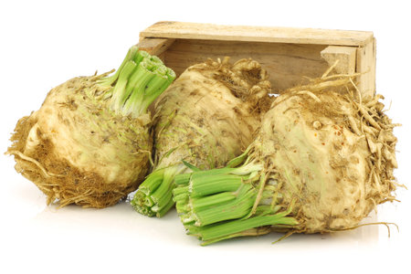 fresh celery roots with some foliage in a wooden crate on a white background 