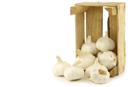 bunch of dried whole garlic bulbs in a wooden crate on a white backgroundの写真素材