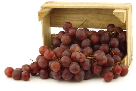 fresh red seedless grapes on the vine in a wooden crate on a white backgroundの写真素材