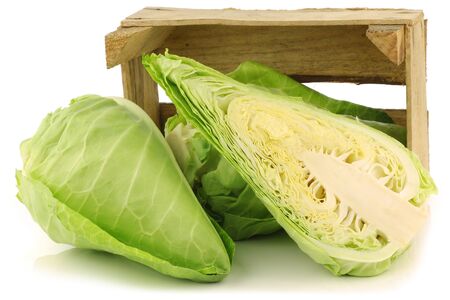 fresh green pointed cabbages and a cut one in a wooden crate on a white backgroundの写真素材