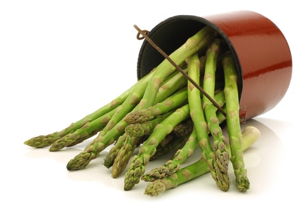 fresh green asparagus shoots in a brown enamel cooking pot on a white backgroundの写真素材