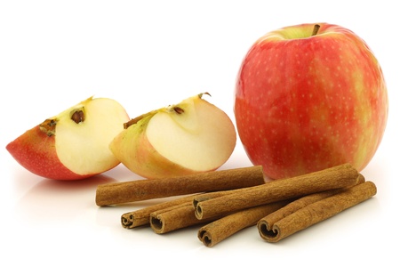 dried cinnamon sticks, a fresh apple and some cut pieces on a white backgroundの写真素材