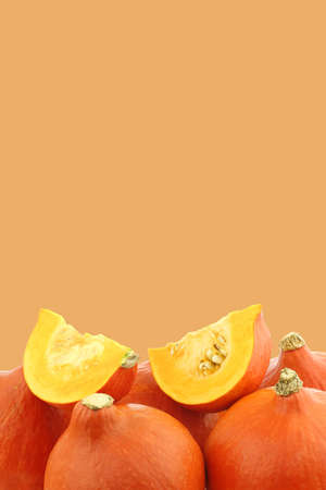 Bunch of orange pumpkins and some cut pieces on an orange backgroundの写真素材