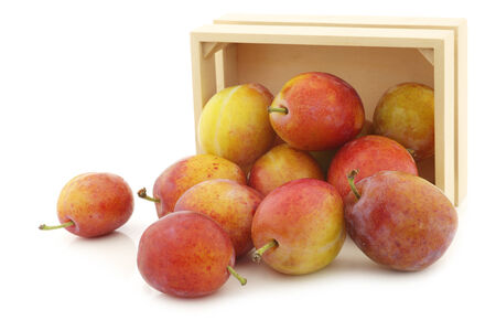 fresh ripe red and yellow plums in a wooden box on a white backgroundの写真素材