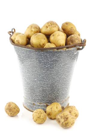 bunch of potatoes in an old enamel bucket on a white backgroundの写真素材