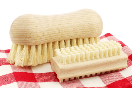 a wooden nail brush and a wooden household brush on a red and white checkered kitchen towel on a white backgroundの写真素材