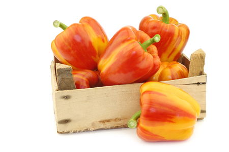fresh orange and yellow enjoya bell peppers (capsicum) in a wooden crate on a white backgroundの写真素材
