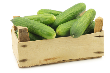fresh green baby cucumbers in a wooden crate on a white backgroundの写真素材