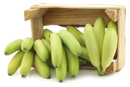 small green snack bananas in a wooden crate on a white backgroundの写真素材