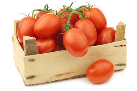 fresh and colorful italian roma tomatoes on the vine in a wooden crate on a white backgroundの写真素材