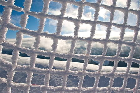 Frozen Mesh Fence with Snow and Cloudy Blue Sky in Backgroundの写真素材