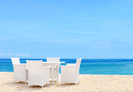Luxury white chairs and table on white sandy beach with a view of blue ocean and clear sky on a bright sunny dayの写真素材