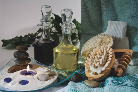 A burning scented candle and two bottles of massage oil, a towel and other utensils massage