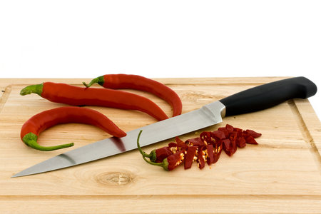 Chili peppers and a kitchen knife lying on a chopping board 