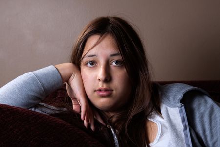 Pretty young brunette hispanic teenage girl with sad serious expression sitting on a sofaの写真素材