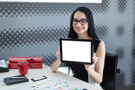 successful young student woman in office holding a tablet and smilingの写真素材