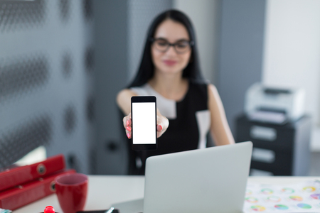 young successful business ladies in the office holding a smartphone and smiling, selective focus on the smartphone, picture with depth of fieldの写真素材