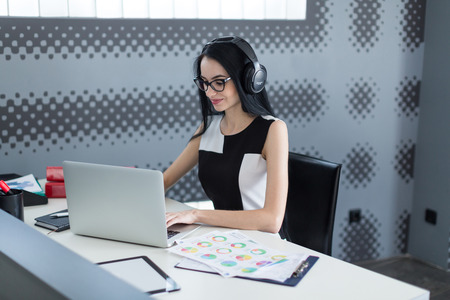 young successful business woman in the office with headphones working at the computerの写真素材