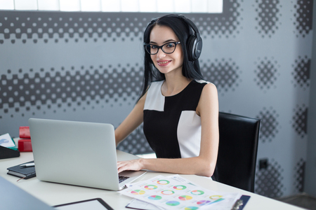 young successful business woman in the office with headphones working at the computerの写真素材