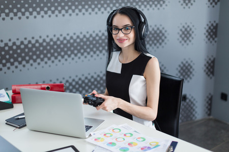 young successful business woman in the office with headphones and with a joystick playing computer gameの写真素材