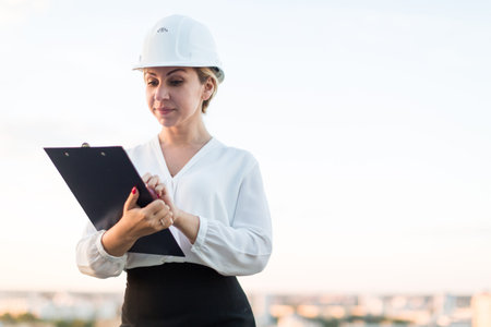 woman engineer in a helmet stands with a folder on the background of the city