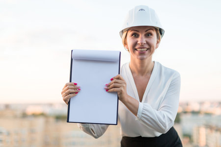 Young woman engineer in a helmet with a folder is a folder on the background of the city