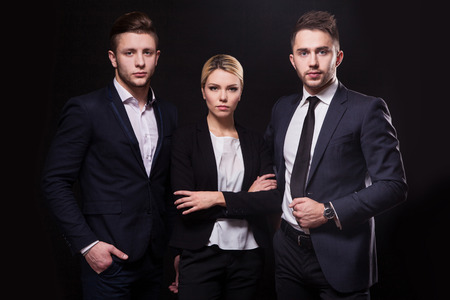 Team of three successful stylish young lawyers on a black background, a woman and two men businessmenの写真素材