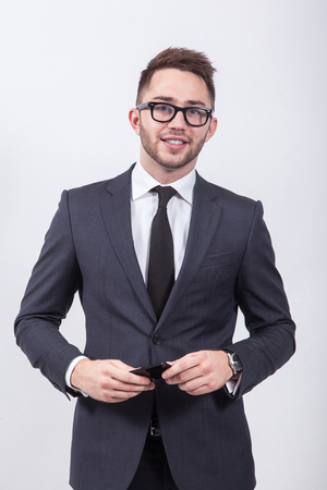 Young successful and confident man on a white background simple elegant business suit with a tie and glasses for vision holds a mobile phone.の写真素材