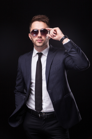 stylish, trendy businessman in a business suit and sunglasses on a black background is confidently looking into the camera.の写真素材