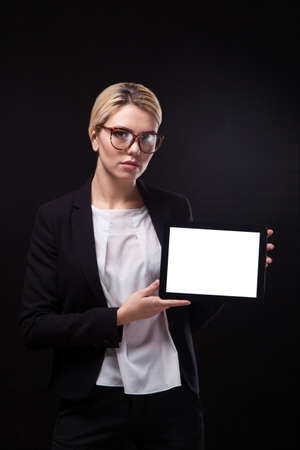successful young businessman woman in a stylish black business suit and a white blouse on a black background confident holding tablet display forward and smiling.の写真素材
