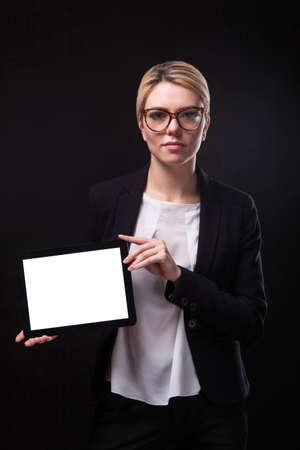 successful young businessman woman in a stylish black business suit and a white blouse on a black background confident holding tablet display forward and smilingの写真素材
