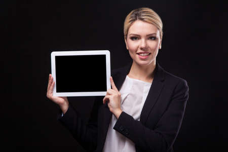 successful young businessman woman in a stylish black business suit and a white blouse on a black background confident holding tablet display forward and smilingの写真素材