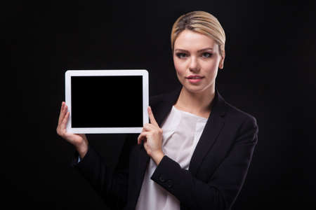 successful young businessman woman in a stylish black business suit and a white blouse on a black background confident holding tablet display forward and smilingの写真素材