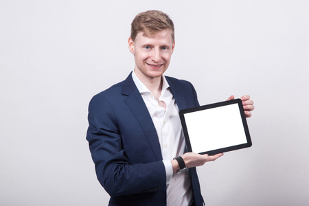 young student in a blue jacket on a white background holding a the tablet screen forward and smiling.の写真素材