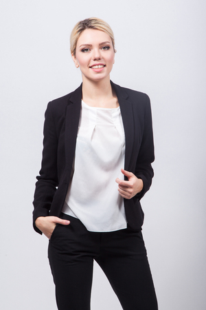 Business lady blonde in black stylish suit standing on a white background and smilingの写真素材