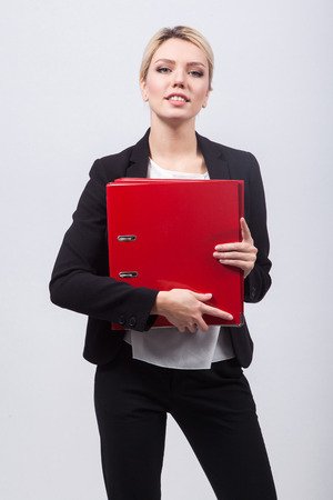 Woman secretary in a black business suit on a white background holding a red office folders.の写真素材