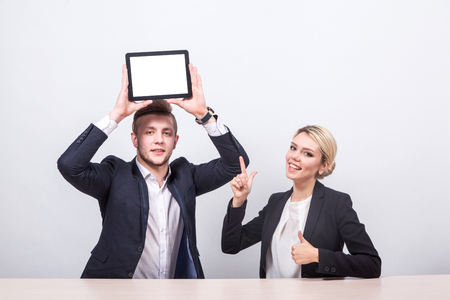 Two students in the classic suit sitting at a table with smiles on their faces and are looking at the camera, man holding her head over a tabletの写真素材