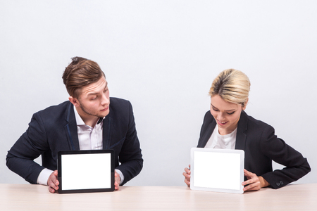 man and woman business people sitting at the table and stare into each other's screens tablets.の写真素材