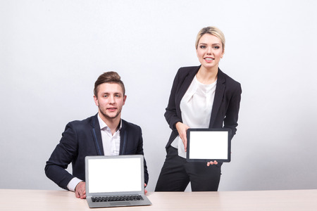 Male businessman sitting at the table and shows the viewer screen laptop blond woman in a business suit shows the screen of the tabletの写真素材