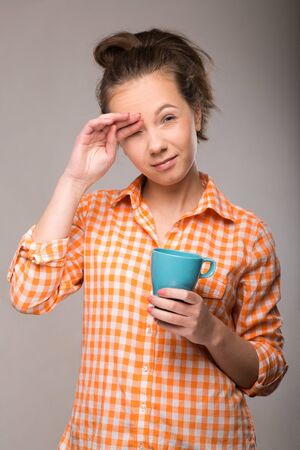 a young housewife in an orange shirt with a cup of coffee in hand on gray backgroundの写真素材