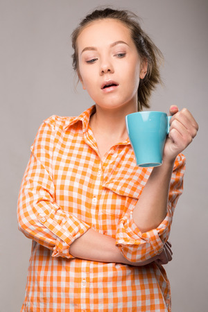 a young housewife in an orange shirt with a cup of coffee in hand on gray backgroundの写真素材