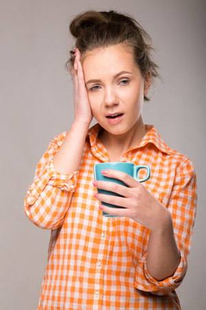 a young housewife in an orange shirt with a cup of coffee in hand on gray backgroundの写真素材