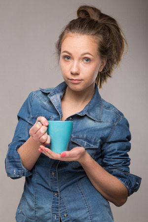 sleepy student with a cup of coffee in hand on studio backgroundの写真素材
